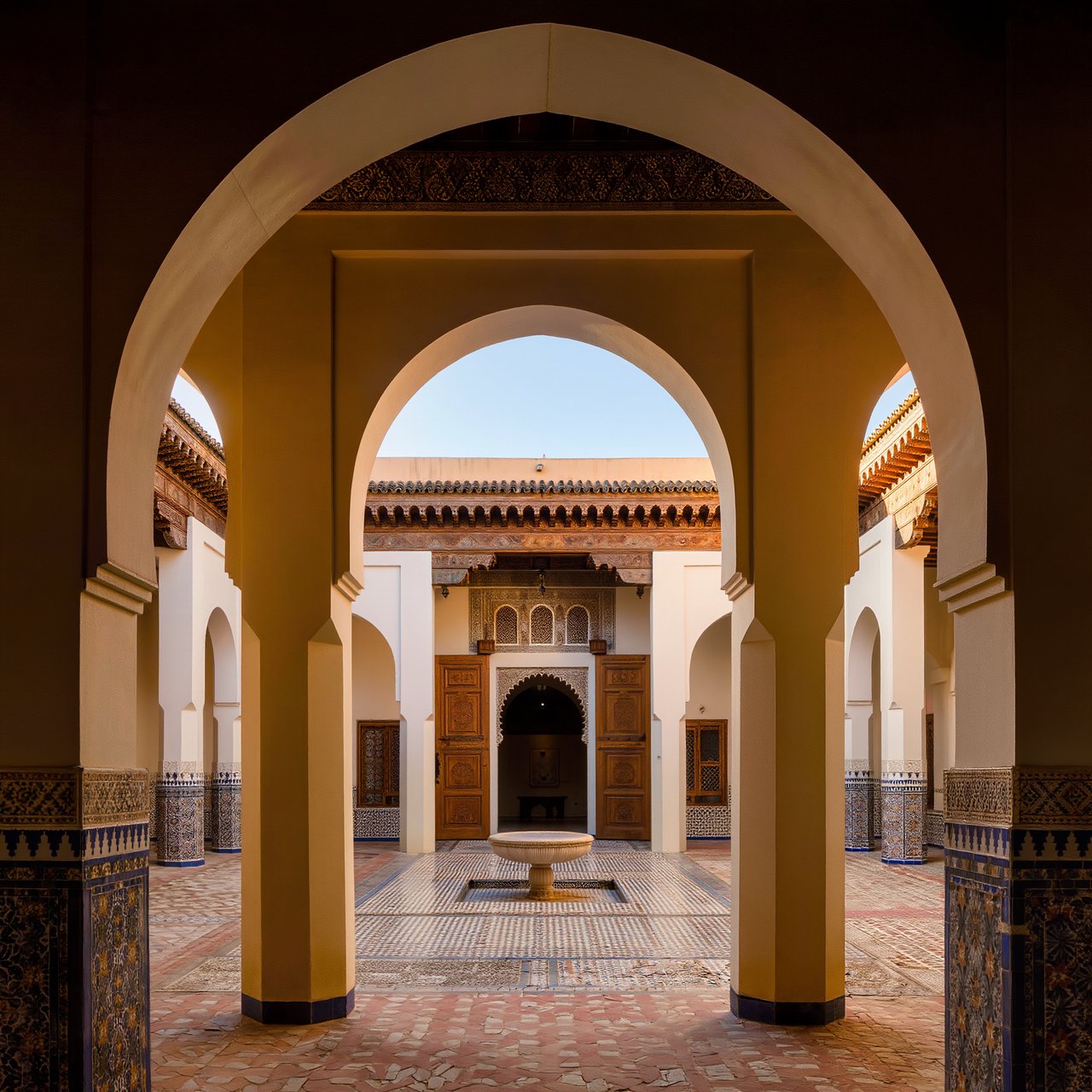 From a shaded courtyard entrance, Moorish Revival residences enclose a tiled fountain court, with cream stucco, carved cedar doors, and blue ceramic bands; late sunlight filters through arcades, revealing aligned walls and credible supports. — Kling v3