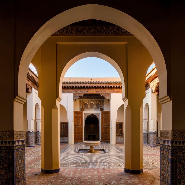 From a shaded courtyard entrance, Moorish Revival residences enclose a tiled fountain court, with cream stucco, carved cedar doors, and blue ceramic bands; late sunlight filters through arcades, revealing aligned walls and credible supports. — Kling v3
