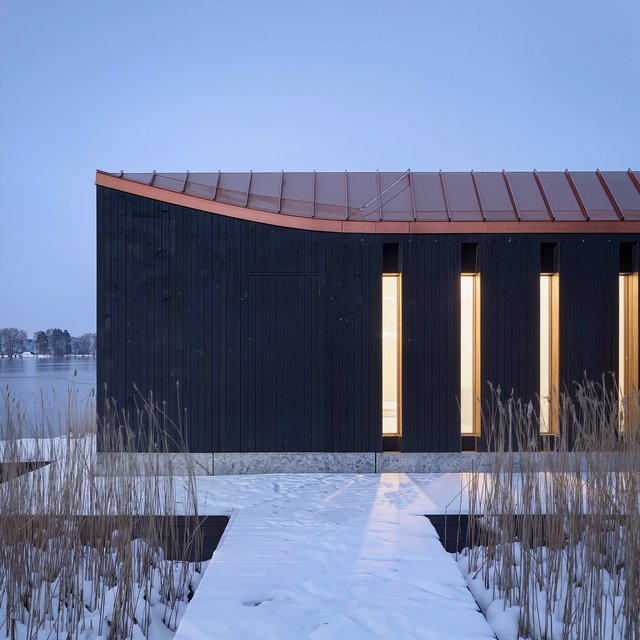 Exterior of a Scandinavian modernist lakeside sauna pavilion, blackened timber cladding, pale granite plinth, copper roof, winter blue-hour light glowing through narrow windows, viewed from a snowy reed-lined path, straight structural geometry and plausible construction. — Kling v3