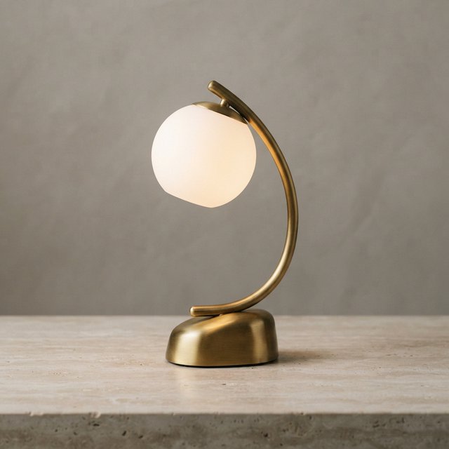 Commercial product photograph of an unbranded sculptural desk lamp made from brushed brass and opal glass, resting on pale travertine, against a warm gray background, with soft diffused light from upper left and gentle grounding shadow. — Nano Banana 2 Lite