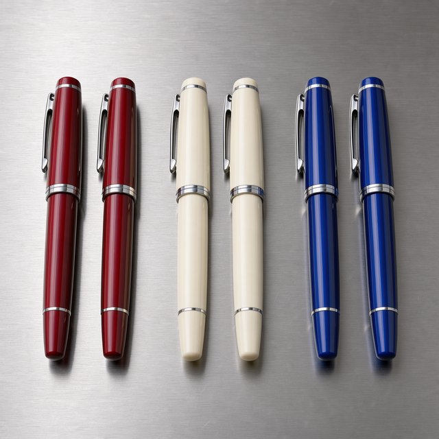 Across a brushed steel counter, exactly six fountain pens rest in three groups: two crimson pens on the left, two ivory pens in the center, and two cobalt pens on the right; nothing else. — FLUX 3 Image