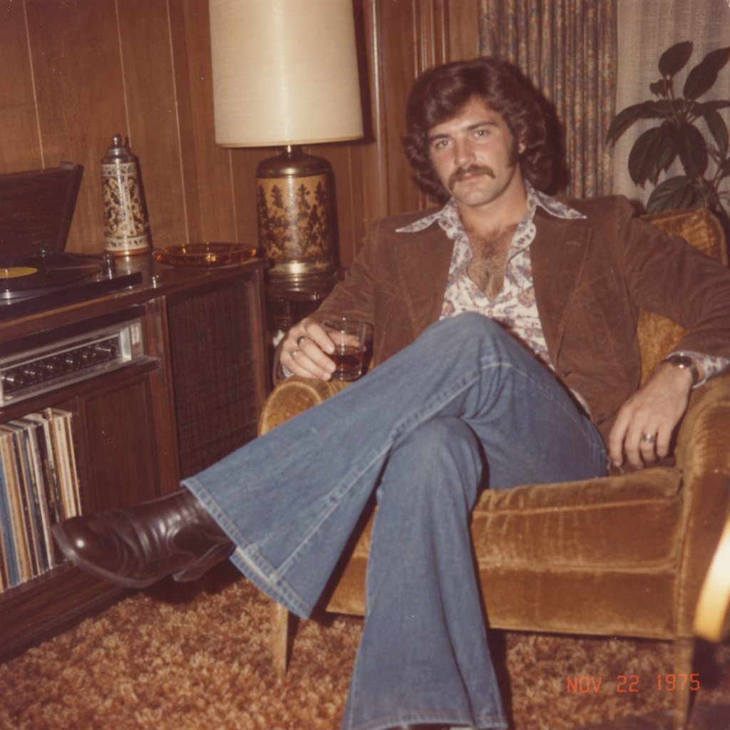 Create an image of a man in the quintessential style of 1975. Style his hair, clothing, accessories, and surroundings to reflect the distinctive look of the mid-1970s—featuring bold silhouettes, eye-catching accessories, layered details, and characteristic colors and textures. Give the image the feel of an authentic 1975 photograph, complete with analog film grain, faded colors, direct flash lighting, and a slight soft-focus effect. Add a period-accurate, red-orange date stamp in a 1970s style in one of the bottom corners. No recognizable posters. No modern objects or text. — GPT Image 2.5 Sunburst