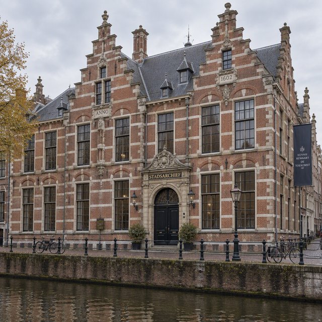Exterior of a Dutch Renaissance canal-side archive, with warm red brick, pale stone bands, stepped gables, and tall sash windows; soft overcast light reveals the masonry, viewed from the opposite quay, with convincing structure and precise architectural lines. — GPT Image 2.5 Sunburst