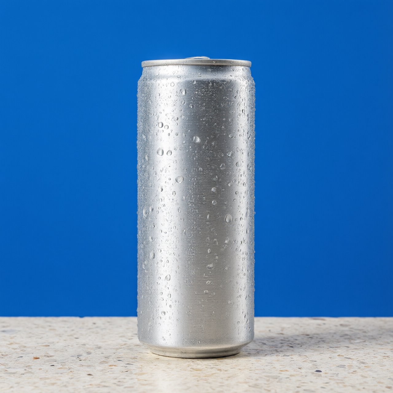 A slim, unbranded sparkling-water can of brushed aluminum, beaded with condensation, stands on a pale terrazzo surface against a seamless electric-blue background; broad overhead diffusion and a crisp side strip create clean highlights, with no lettering or graphics. — Qwen Image 3.0