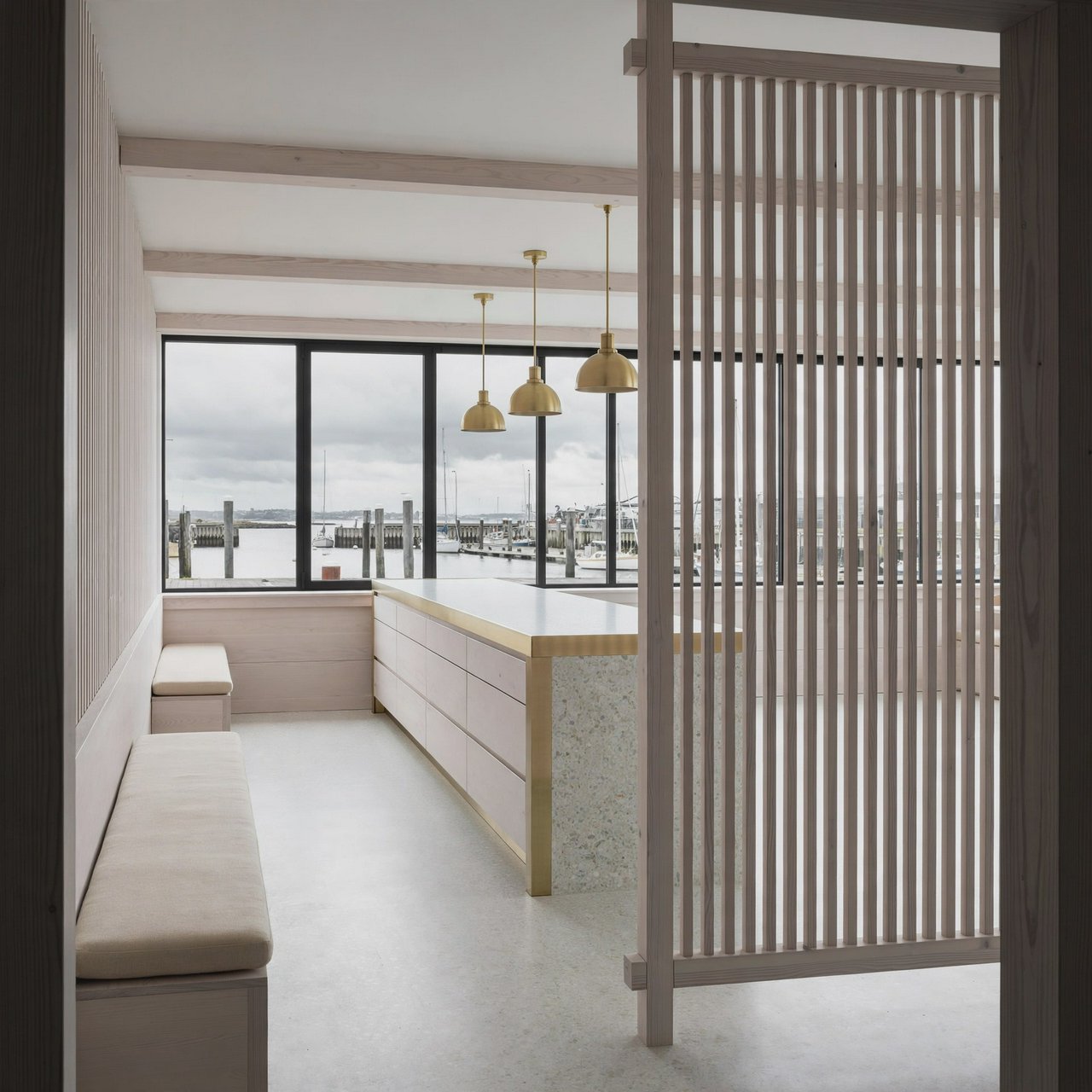 Inside an empty harbor café, restrained Danish modern design pairs ash slat screens, pale terrazzo, and brushed brass; overcast window light reaches the counter, viewed from the entrance, with aligned joinery and believable supports. — Muse Image 1.0