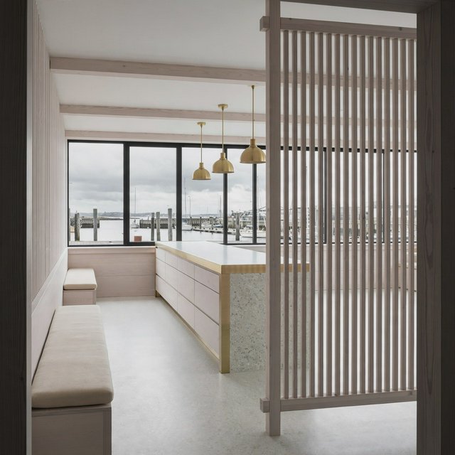 Inside an empty harbor café, restrained Danish modern design pairs ash slat screens, pale terrazzo, and brushed brass; overcast window light reaches the counter, viewed from the entrance, with aligned joinery and believable supports. — Model 14