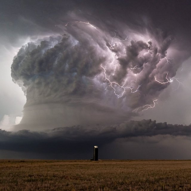 A supercell thunderstorm over flat farmland, lightning inside the cloud, a lone grain silo, dramatic but realistic. — Krea 2 Large