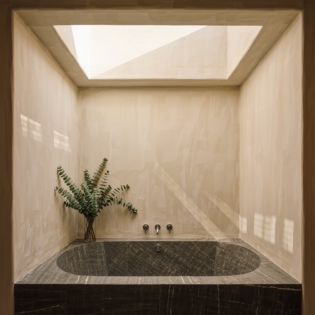 A spa bathroom with a stone tub, a skylight, plaster walls in warm white, eucalyptus in a vase, soft shadows. — Kling v3 Omni