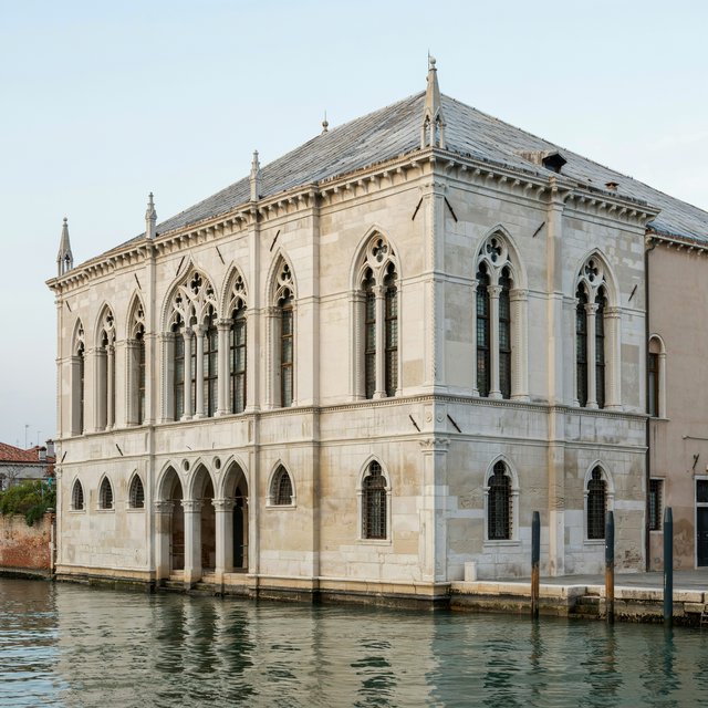 Exterior of a Venetian Gothic opera house beside a quiet canal, pale Istrian limestone, pointed arches, quatrefoil tracery, and a steep slate roof; cool morning light, viewed from across the water, crisp masonry lines and believable structure. — Ideogram v4.5