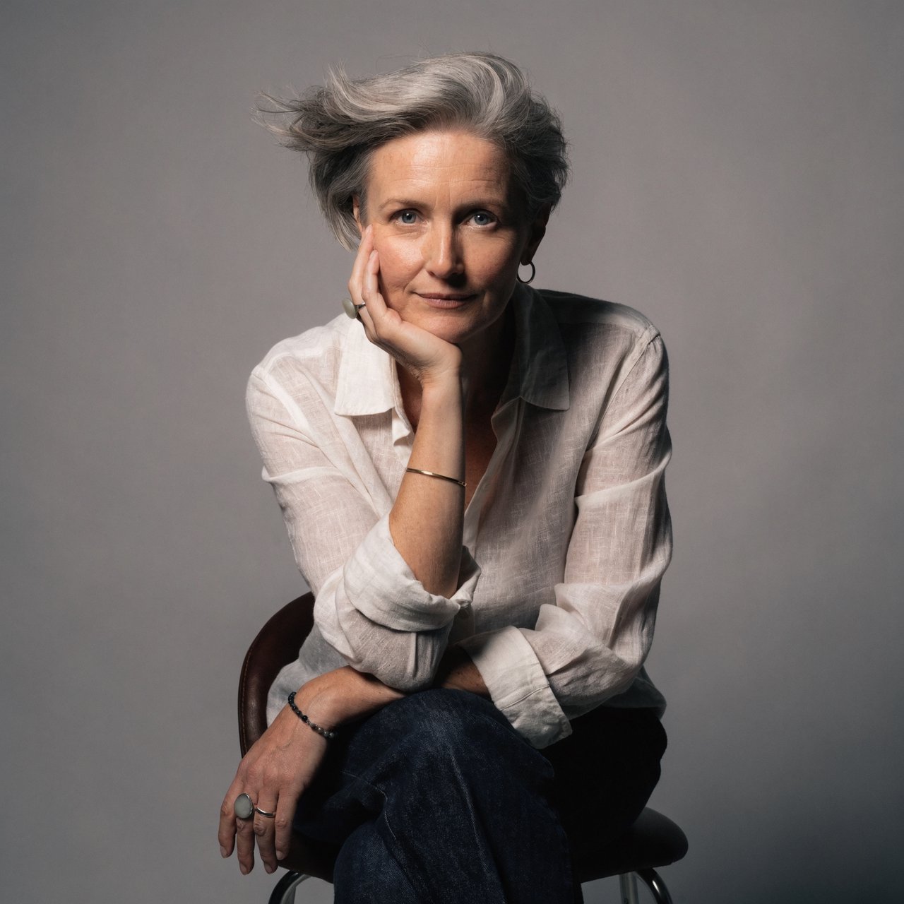 Studio portrait of a woman in her 40s with short grey hair and a linen shirt, Rembrandt lighting, neutral grey backdrop, slight smile. — Recraft v4 Pro