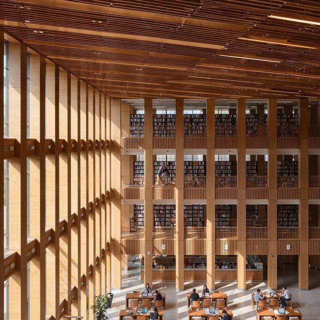 Interior of a modern public library with a three-storey atrium, timber ceiling slats, people reading, afternoon light through a glass wall. — Kling v3