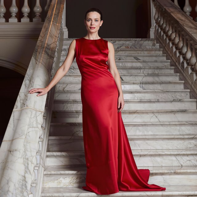An adult woman in a floor-length red satin evening gown on a marble staircase, soft key light, confident pose, magazine cover style. — Kling v3