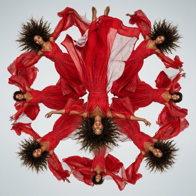 Image of a pop-dance African-American diva. The woman hangs completely inverted in mid-air, head pointing toward the floor and legs toward the ceiling. Her huge hair falls and spreads dramatically in the opposite direction, while her expression remains cool and composed. Her red gown is turned inside out, exposing its sparkling lining, seams, and construction. To push the surrealism further, a second, reversed version of her silhouette appears to peel outward from her original form, like a three-dimensional reflection escaping its owner. Multiple copies of the woman circle around a central point, each rotated to a different angle. Their flowing hair and red gowns form a pinwheel or circular vortex, creating the impression that one woman is spinning endlessly around herself. — Qwen Image 3.0