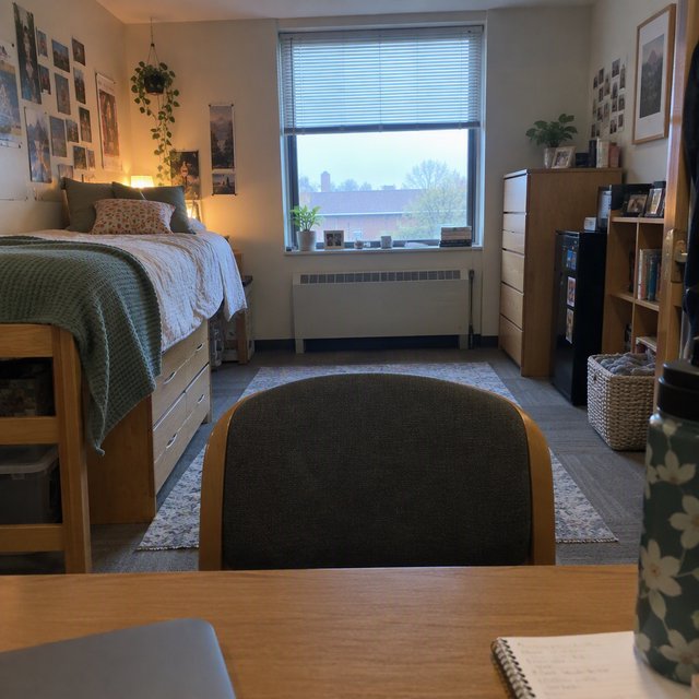 A dorm room belonging to an adult woman, photographed with a cell phone. The camera is sitting on a desk facing the empty chair and the rest of the room. — GPT Image 2.5 Flare