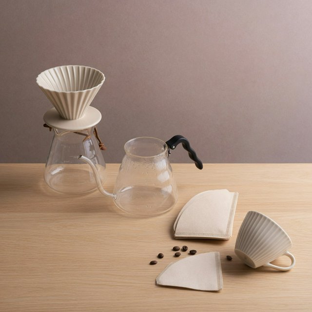 From directly overhead, an unbranded pour-over coffee set with ribbed porcelain and clear borosilicate components arranged in sequence on pale oak; warm taupe background, broad diffused softbox light and gentle side fill shape this commercial product image, no lettering. — Model 6