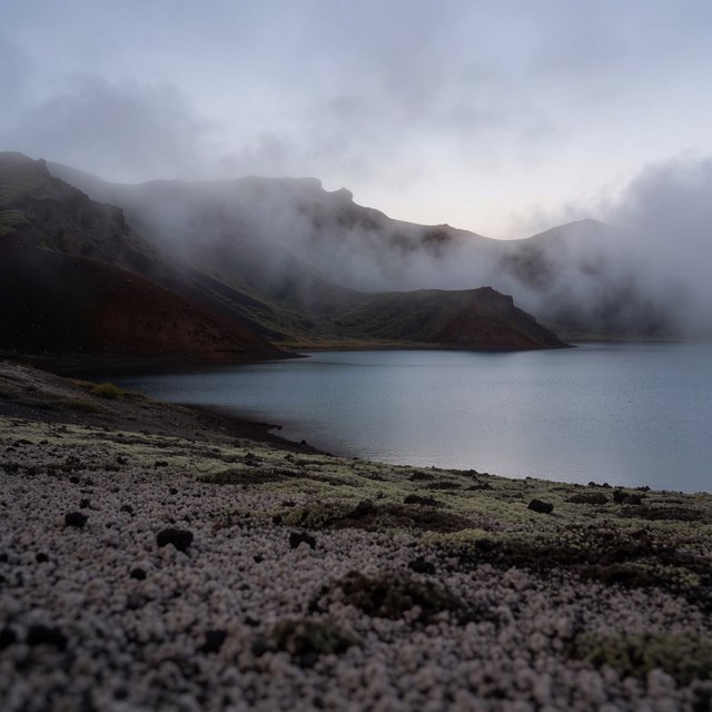 At first light, a rain-cleared volcanic caldera lake lies beneath thinning fog; pumice grains and damp lichen sharpen the near shore, while dark cinder slopes step back toward a distant rim. — Krea 2 Medium