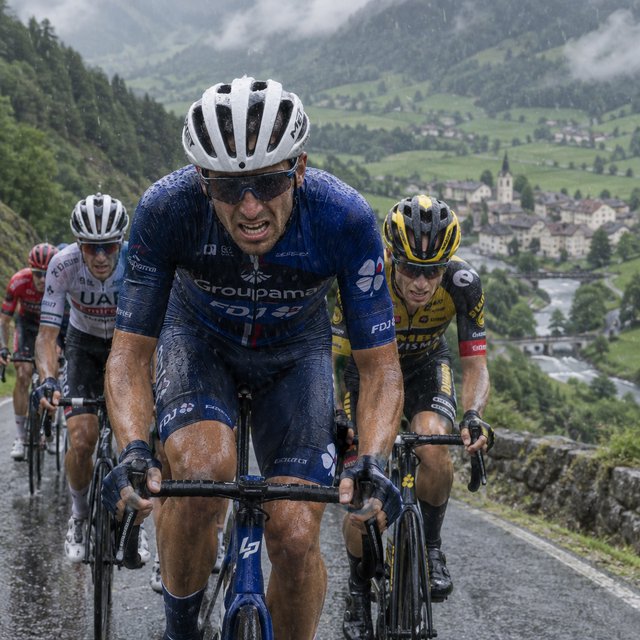 A frontal, close-up shot of a field of competitive cyclists ascending a mountain in the rain. In the background, we see a lush green valley with a small town. — GPT Image 2.5 Flare