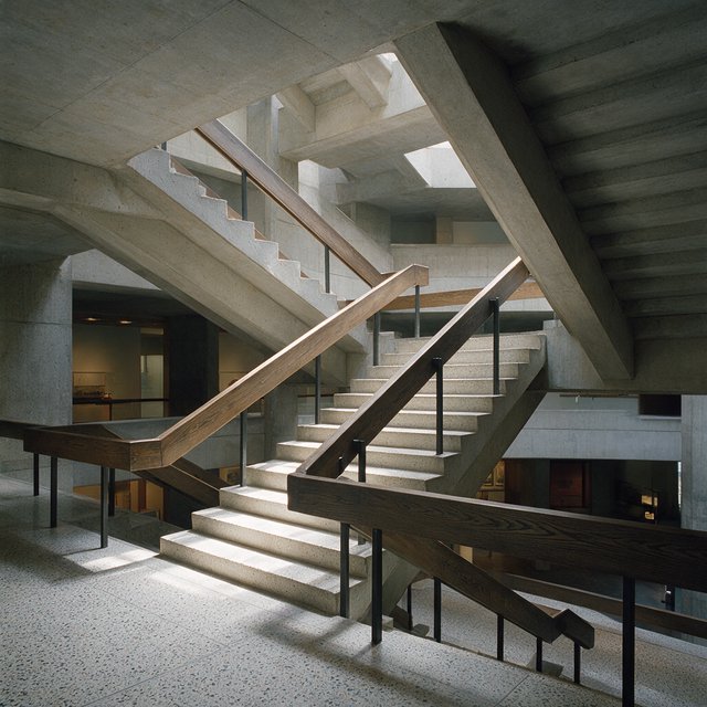 At the heart of a restrained Brutalist museum, a folded concrete stair rises beside smoked-oak handrails and terrazzo landings; skylight washes the treads, seen from the lower landing, with aligned flights and believable supports. — Seedream 5.0 Pro