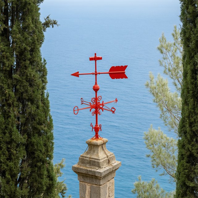 At a coastal overlook, a small red weather vane stands on a stone post. Exactly two dark-green pine trees line the left edge and one pale-green pine tree stands at the right edge; a blue sea fills the background, nothing else. — Model 17