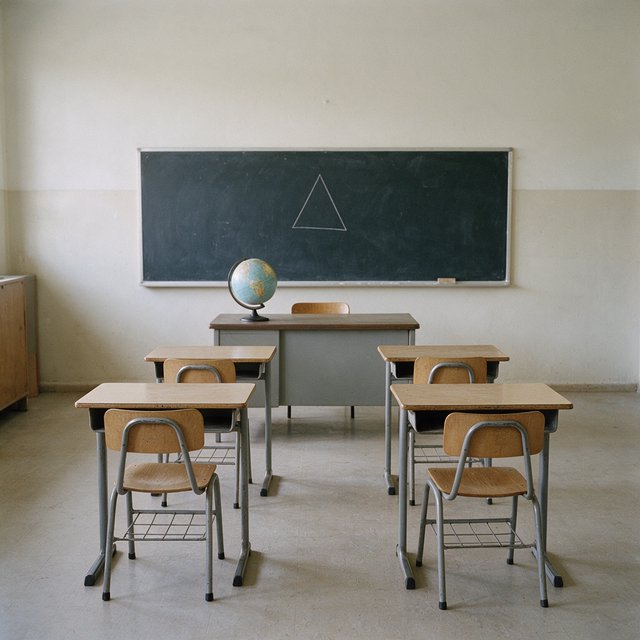 A classroom with exactly four desks in two rows, a globe on the teacher's desk, a chalkboard with a single drawn triangle, empty of people. — Seedream 5.0 Pro