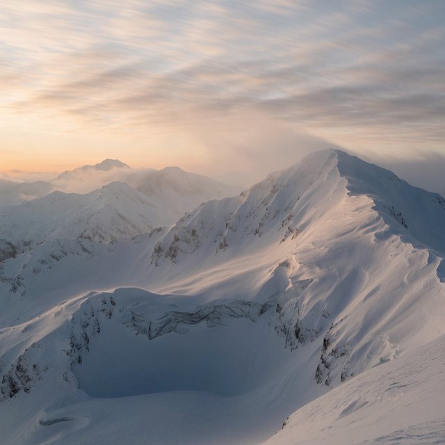 Wind combs a high granite ridge above a glacial cirque at sunrise, beneath clearing snow squalls; granular rime crusts foreground boulders while successive peaks dissolve into blue cloud shadow. — Krea 2 Medium
