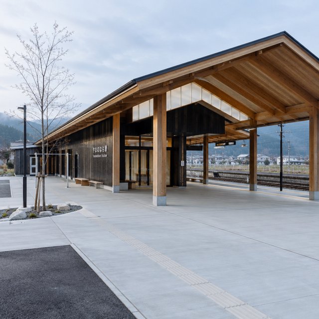 Contemporary Japanese timber train station, charred cedar cladding, pale concrete platform, broad pitched roof with exposed beams and translucent clerestories, cool morning light, viewed obliquely from the quiet approach plaza, precise straight lines and plausible structure. — GPT Image 2.5 Flare