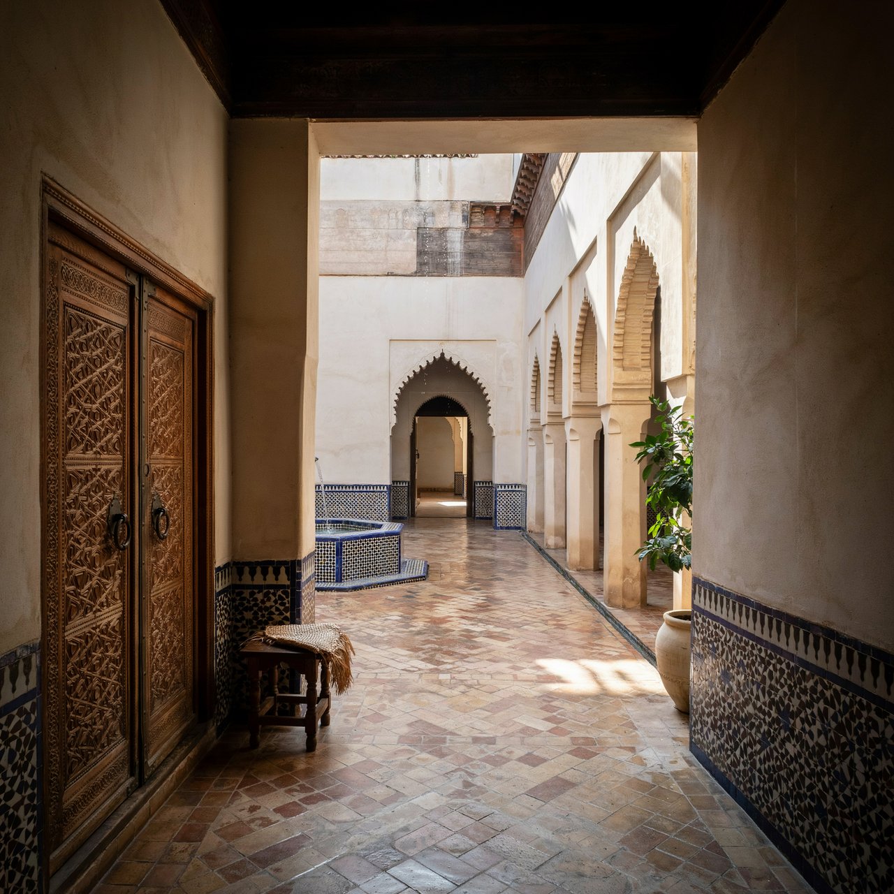From a shaded courtyard entrance, Moorish Revival residences enclose a tiled fountain court, with cream stucco, carved cedar doors, and blue ceramic bands; late sunlight filters through arcades, revealing aligned walls and credible supports. — Ideogram v4
