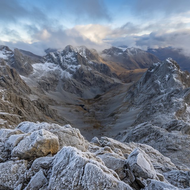 Wind combs a high granite ridge above a glacial cirque at sunrise, beneath clearing snow squalls; granular rime crusts foreground boulders while successive peaks dissolve into blue cloud shadow. — Qwen Image 3.0