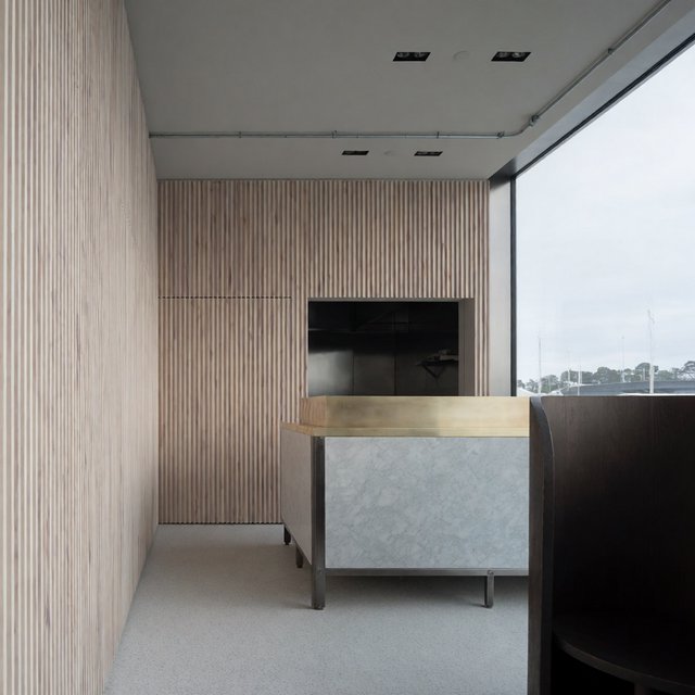 Inside an empty harbor café, restrained Danish modern design pairs ash slat screens, pale terrazzo, and brushed brass; overcast window light reaches the counter, viewed from the entrance, with aligned joinery and believable supports. — Model 12