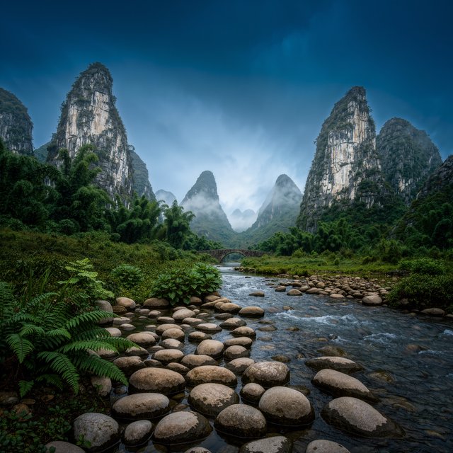 A limestone karst valley at blue hour after a light shower, towering pale cliffs rising above a clear river, low clouds snagging on pinnacles, slick ferns and rounded pebbles leading toward a distant stone arch. — Kling v3 Omni