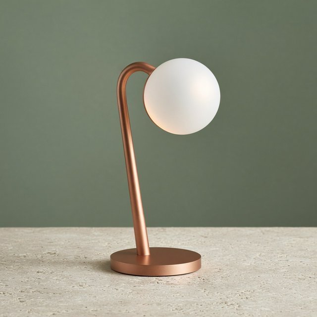Commercial product photograph of an unbranded sculptural desk lamp with a frosted opal glass globe and brushed copper stem, standing on a pale travertine surface against a muted sage background, illuminated by soft overhead diffusion and a delicate warm rim light. — Grok Imagine Image 2