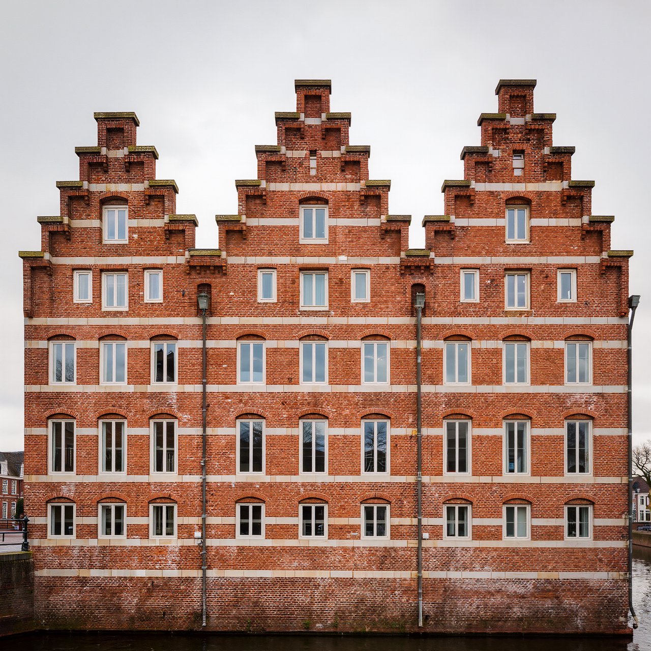 Exterior of a Dutch Renaissance canal-side archive, with warm red brick, pale stone bands, stepped gables, and tall sash windows; soft overcast light reveals the masonry, viewed from the opposite quay, with convincing structure and precise architectural lines. — Kling v3