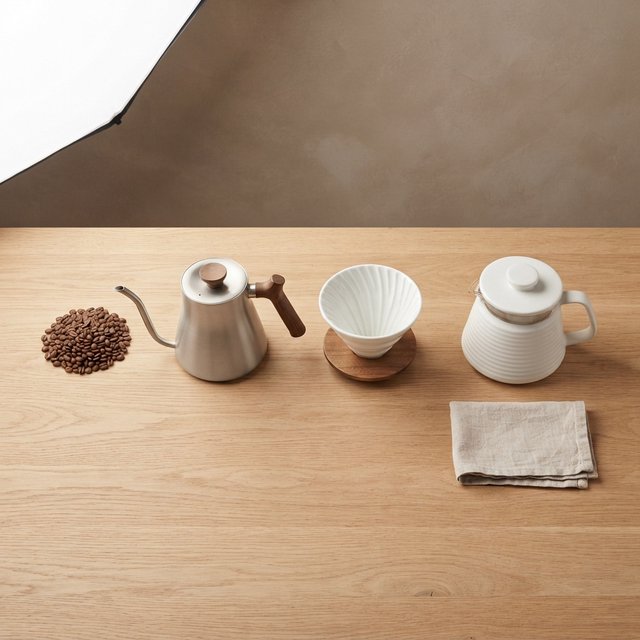 From directly overhead, an unbranded pour-over coffee set with ribbed porcelain and clear borosilicate components arranged in sequence on pale oak; warm taupe background, broad diffused softbox light and gentle side fill shape this commercial product image, no lettering. — Model 16