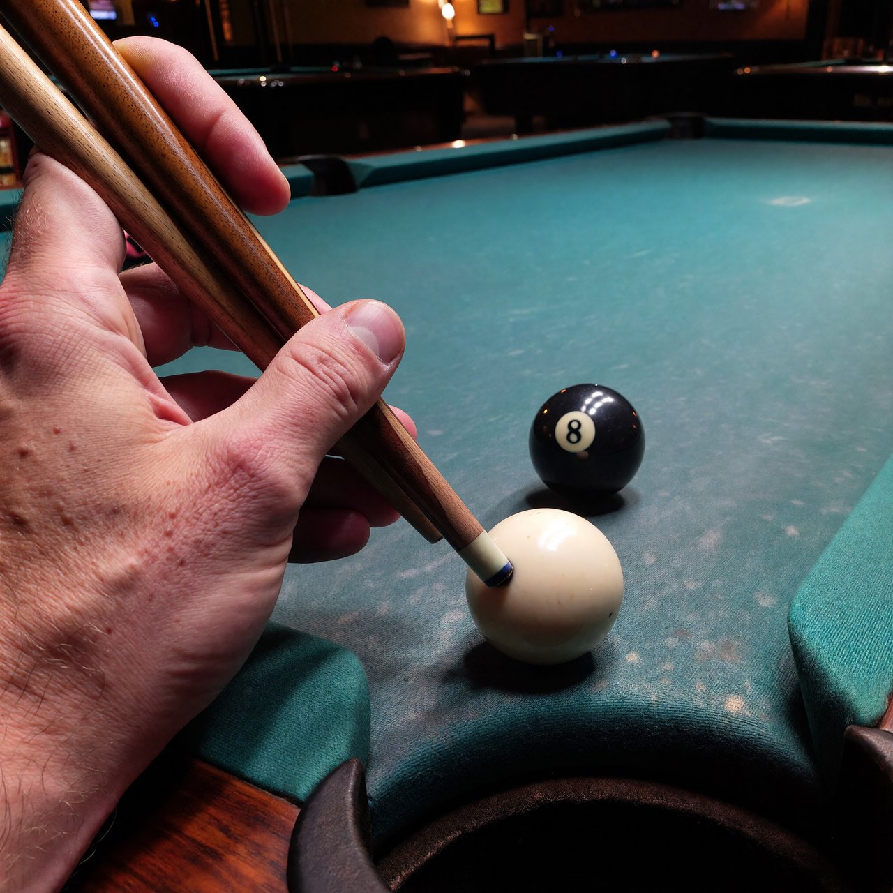 First-person perspective of an adult pool player’s left hand holding the cue, aiming the white cue ball at the black 8-ball and intending to pocket it in the center pocket. — ImagineArt 1.5 Pro