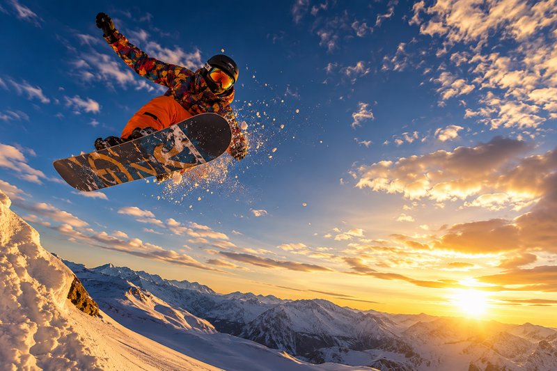 Snowboarder in orange jacket performing a high jump over snowy ridge at sunset