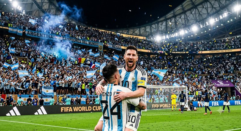 Argentina players celebrate with embrace amid cheering fans and blue-white banners.