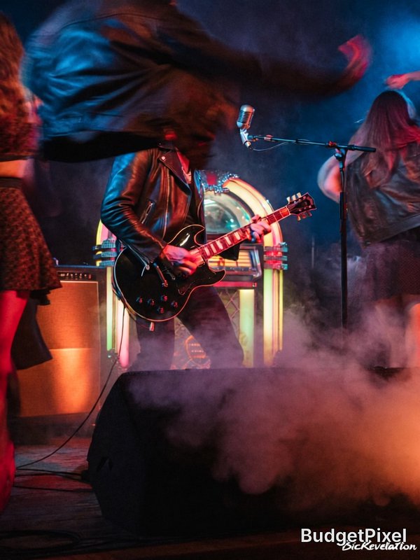 Live concert shot of leather-jacketed guitarist playing electric guitar on smoky neon-lit stage n...