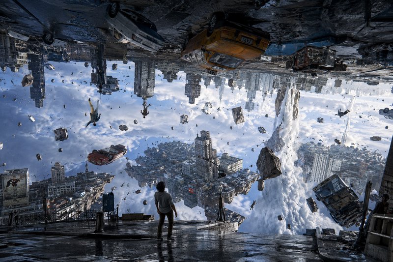 A lone man stands on wet pavement, observing a surreal gravity-broken upside-down city with float...