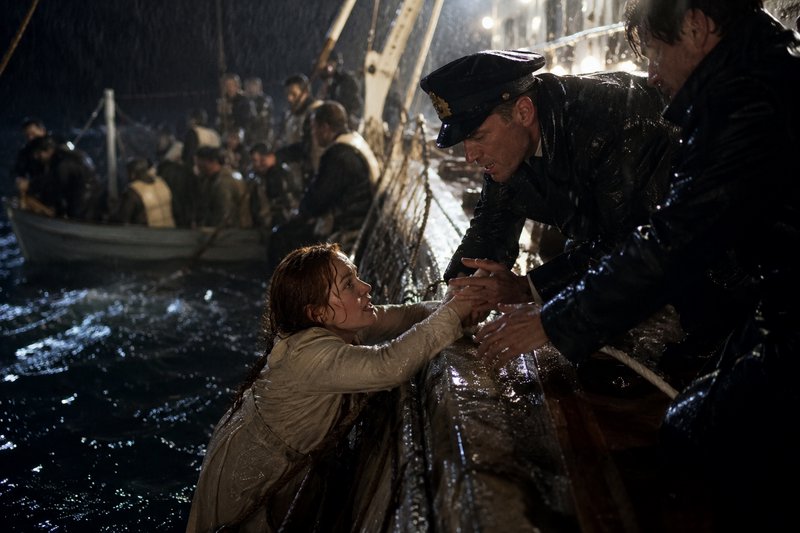 A soaking wet woman reaches up to be pulled aboard a ship from stormy dark ocean during a nightti...