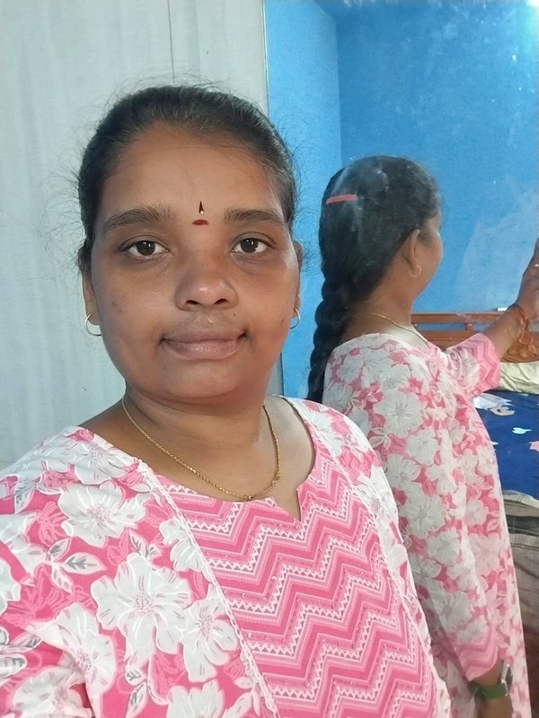 Candid selfie of South Indian woman with red tilak, her mirror reflection visible in a bright hom...