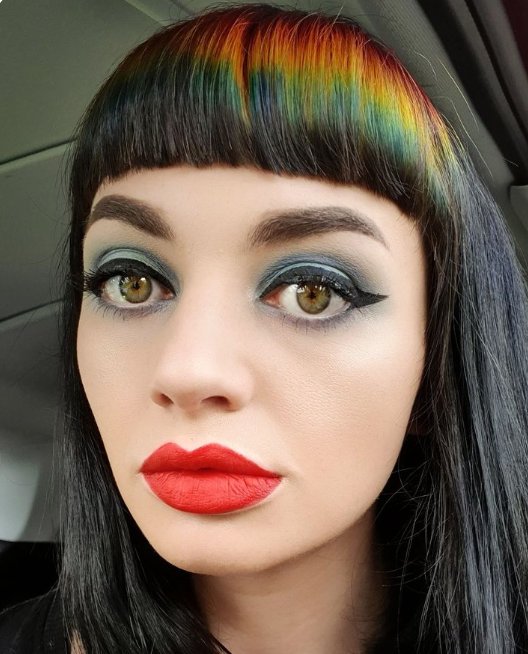 Woman with rainbow bangs and bold makeup in a car interior.