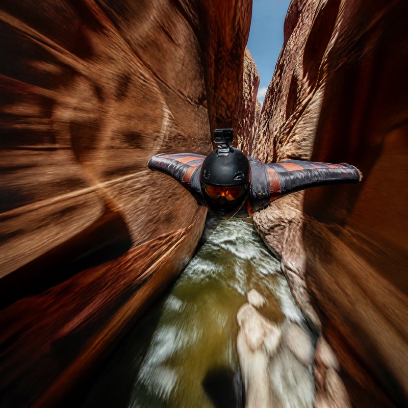 Wingsuit pilot with helmet action cam flies at high speed through narrow sandstone slot canyon ab...