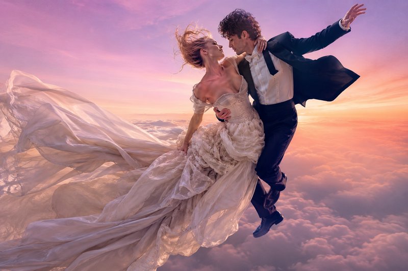 Surreal portrait of a wedding couple floating tenderly above clouds against a pastel pink and pur...