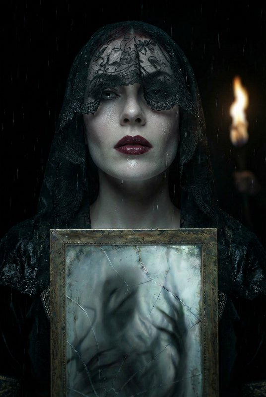 Gothic portrait of a veiled woman holding a cracked mirror in the rain with a torch in the backgr...