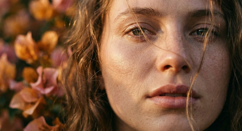 Close-up portrait of a freckled woman with autumn flowers in the background.