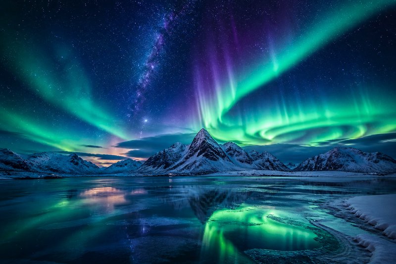 Snowy mountains beneath vibrant green and purple aurora borealis over a calm icy lake.