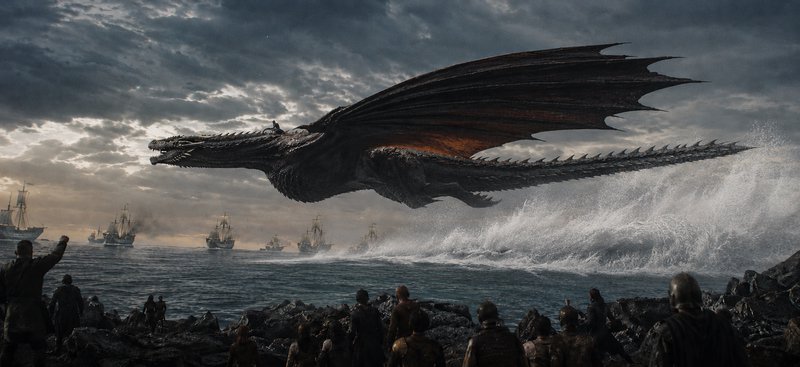 Dark dragon soars above rocky shore unleashing a fiery wake on ships in a dramatic sea battle.