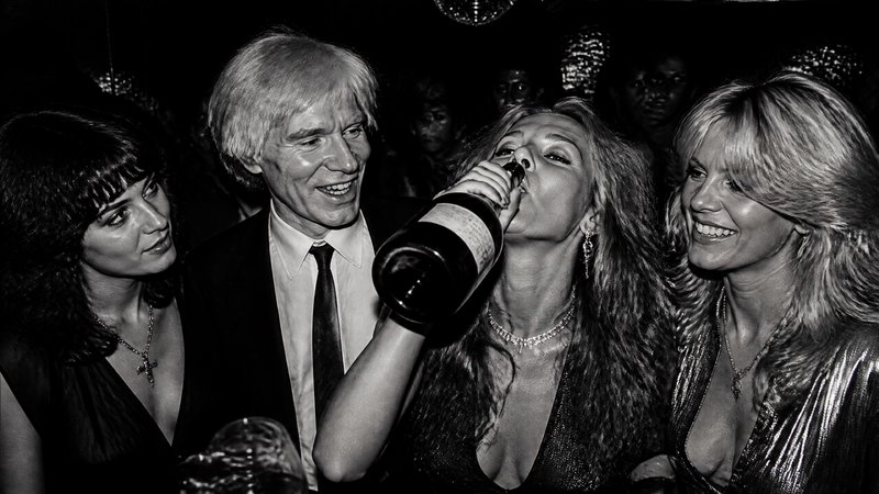 Woman drinks champagne at a glamorous black-and-white party with friends.