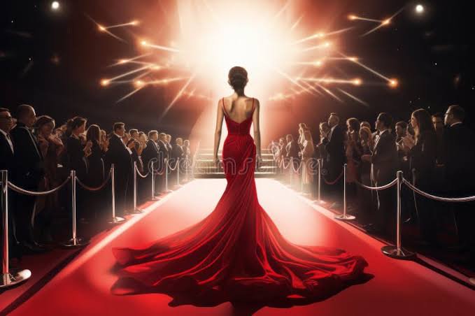 Woman in a flowing red evening gown on a red carpet with spotlights at a gala