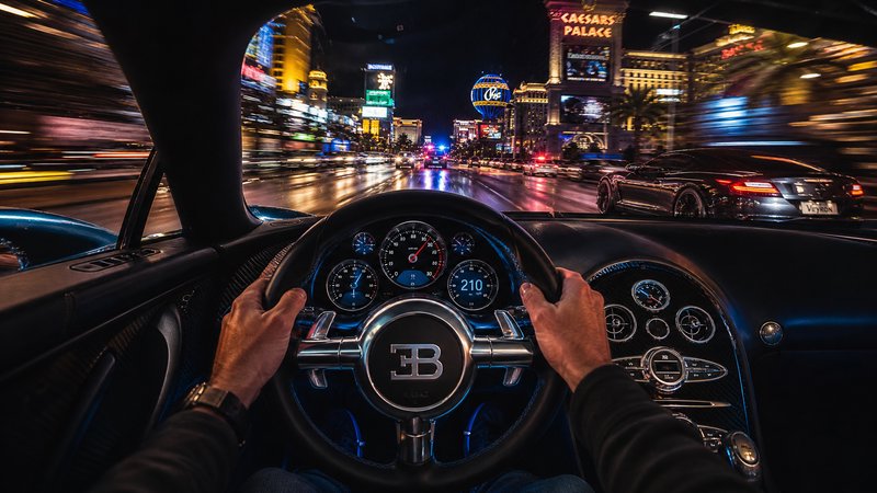 Driver’s view from a luxury Bugatti cockpit on a neon-lit city street at night.